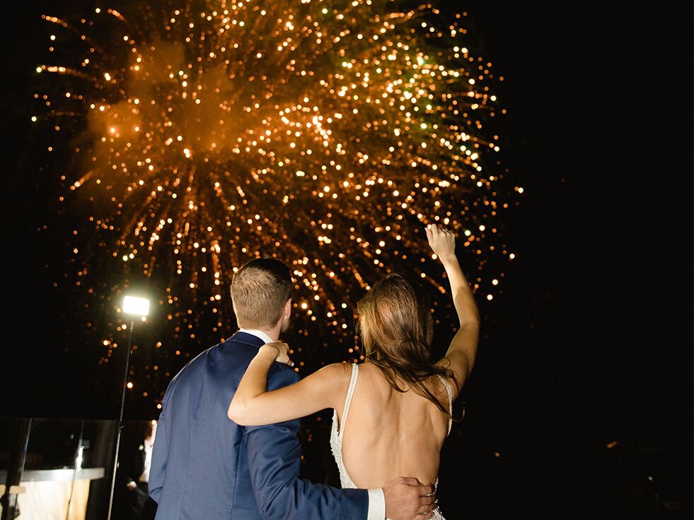 Bride and groom embracing as golden wedding fireworks bloom above them